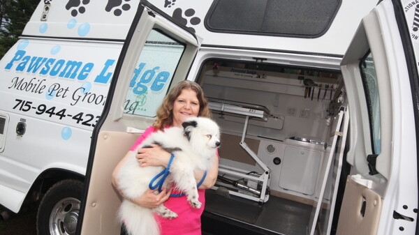 Judy Kippenhan poses with her customized pet-grooming vehicle and a satisfied customer.