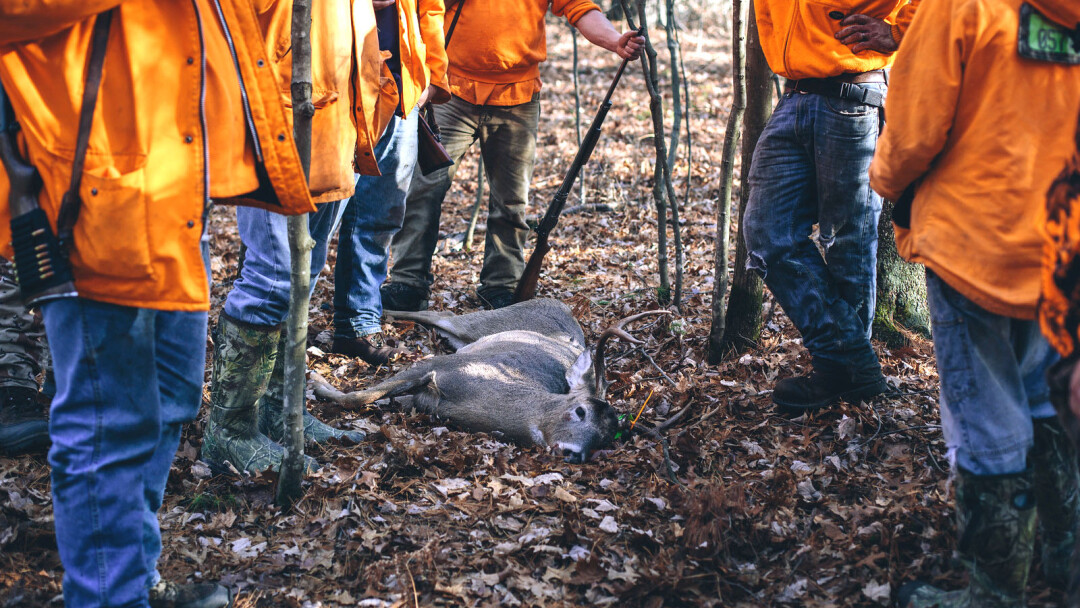 GREAT SHOT. Eau Claire photographer Travis Dewitz (left) chronicled the quintessential northern Wisconsin ritual, deer hunting, in his book Blaze Orange. The many images in the book include hunters gathered around a 10-point buck in the town of Bridge Creek (above) and the mounted heads at Miller’s Antiques in Hixton