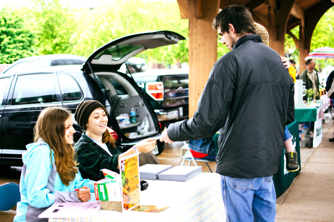 ABOVE: AmericCorps Vista worker Kate Beaton, center, hands out information about the Market Match program at the Downtown Eau Claire Farmers Market. BOTTOM LEFT: The new program is an addition to the existing token program, which allows Food Share participants to buy wooden tokens that can be exchanged for fresh produce.