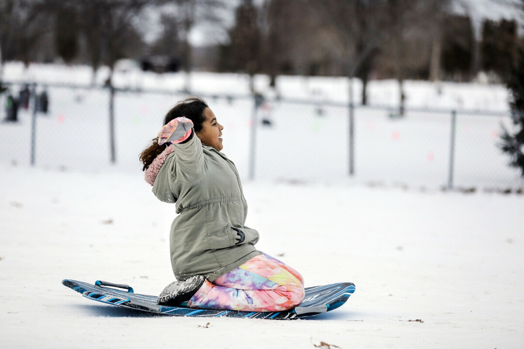 A successful sledder signals her triumph at the foot of Seven Bumps Hill.