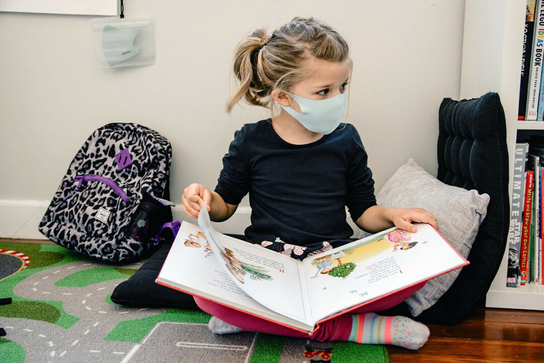 MASK ON, MASK OFF. A child reads a book while wearing a face mask. (Photo by Kelly Sikkema / Unsplash)