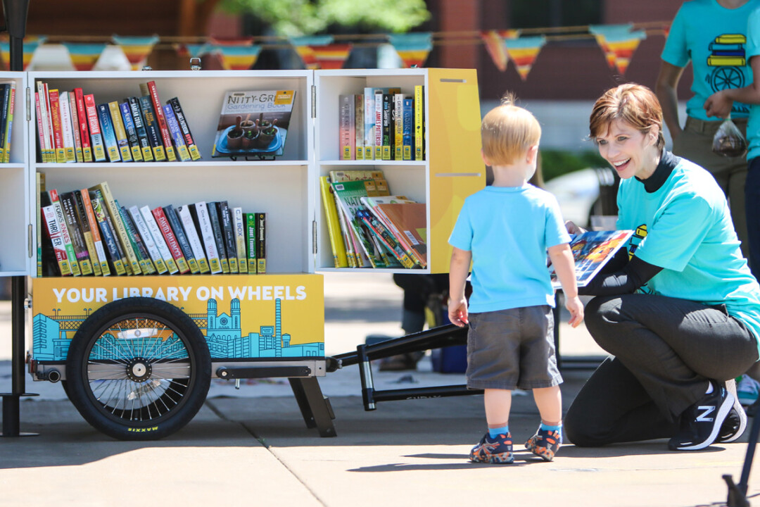 PAGING YOUNG READERS. L.E. Phillips Memorial Public Library Director Pamela Westby shows off the contents of the library’s new BookBike during a jaunt to Phoenix Park on a recent summer morning. The custom-made bike trailer, which can hold about 100 books, will be pedaled to events by librarians.